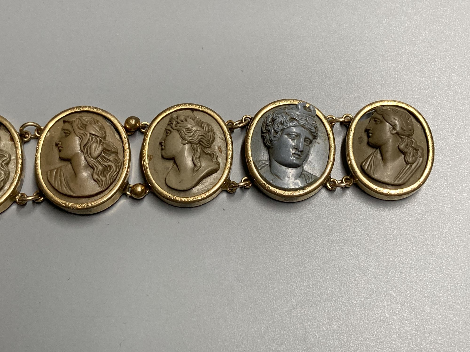 A late Victorian gilt metal bracelet set with seven oval lava plaques carved with busts of ladies, 17cm.